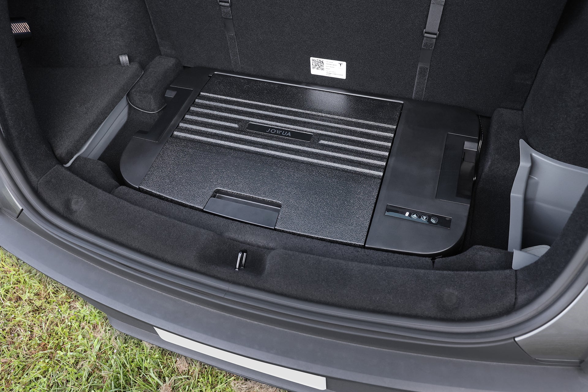 Model Y 的特寫畫面採用了 JOWUA Taiwan Type-C ＆ 點菸器 雙軌車用行動冰箱，這是一款 35 公升的大容量黑色平面儲物冰箱，整合在後車廂地板上，並配備把手與稜紋細節。.
