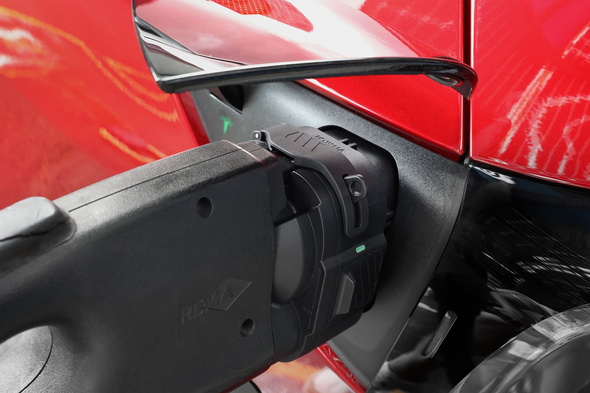 一張特寫照片，顯示一輛紅色電動車正透過黑色 JOWUA 台灣製 CCS1 轉 CCS2 直流與交流快慢充轉接頭進行充電，該轉接頭已高效地連接至車輛的充電接口，以進行電動車充電。.