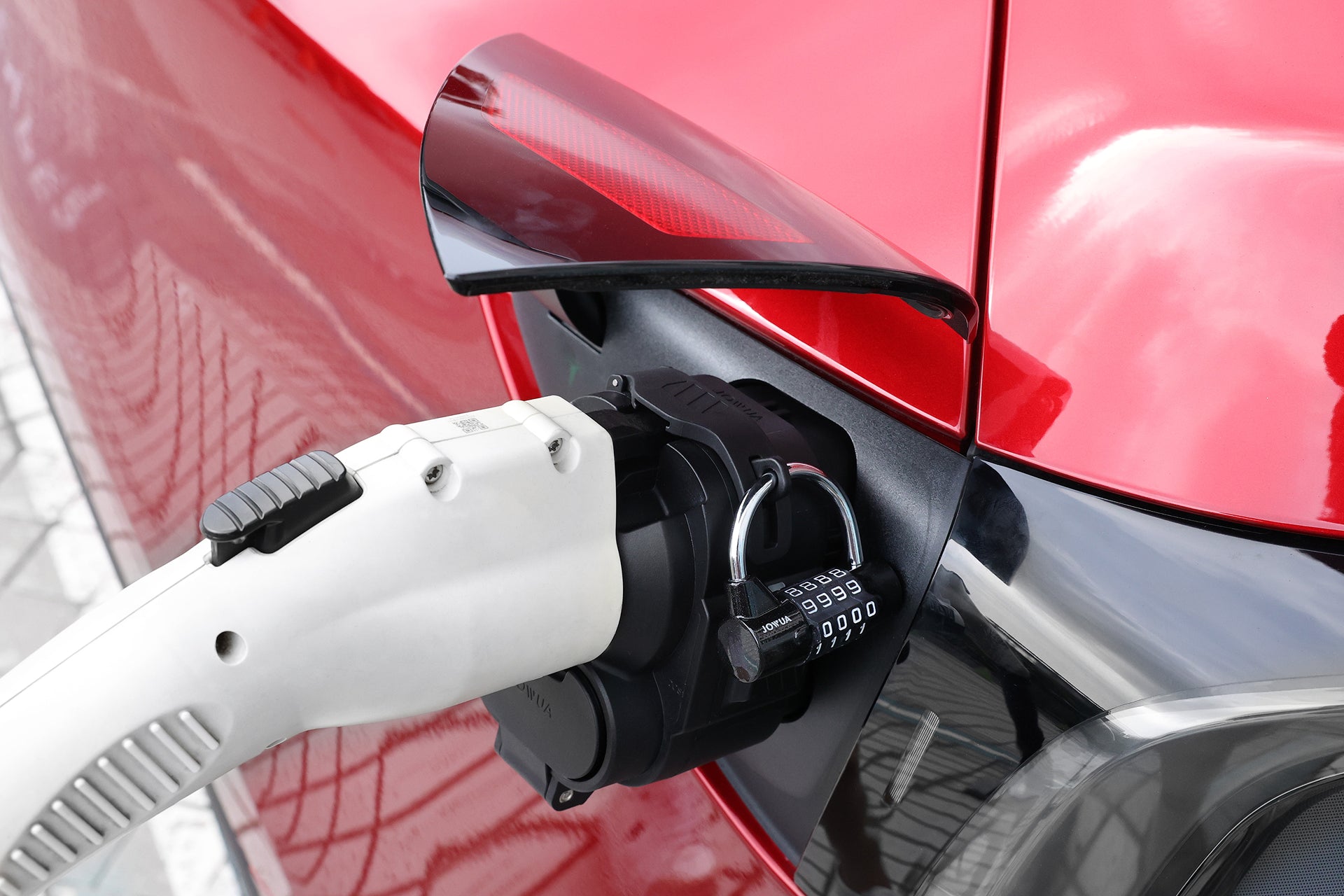 一輛紅色電動車正在使用 JOWUA 台灣製 CCS1 轉 CCS2 直流與交流快慢充轉接頭進行充電的特寫畫面，該轉接頭以組合式掛鎖固定，並搭配白色充電線。.
