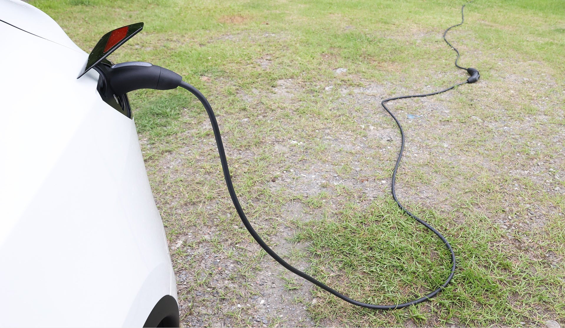 一輛白色電動車停在草地上，插入JOWUA台灣CCS2-AC（2型）電動車充電延長線（5公尺），並進行了防水設計。為了方便起見，長長的黑色電纜連接到終端兼容Type-2充電座。.