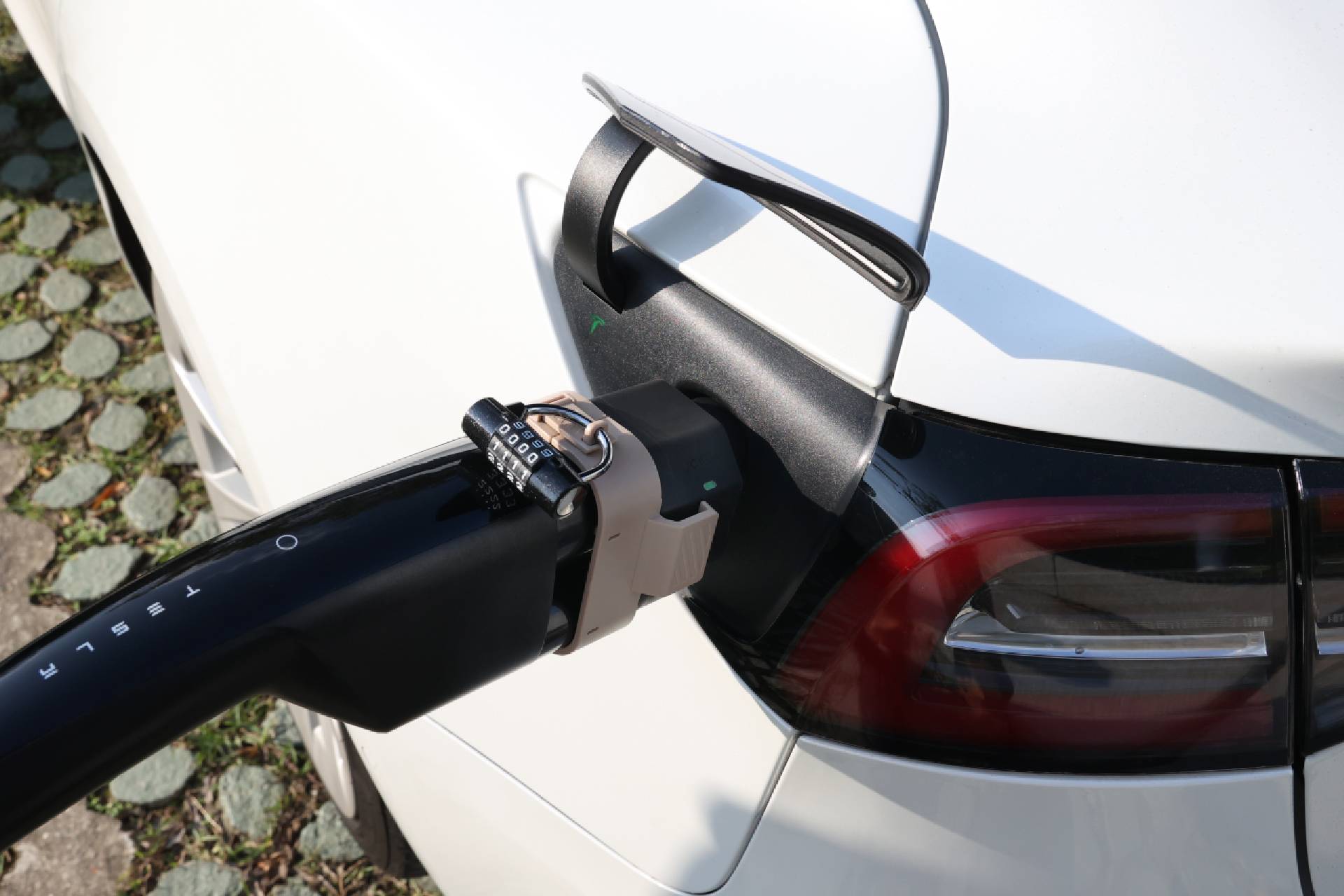 特寫圖顯示一輛 Tesla 正使用 JOWUA Taiwan CCS2 to NACS (TPC) 直流轉接頭充電。在汽車連接埠附近的充電電纜上，繫著一隻棕色腕表和黑色掛鎖。.