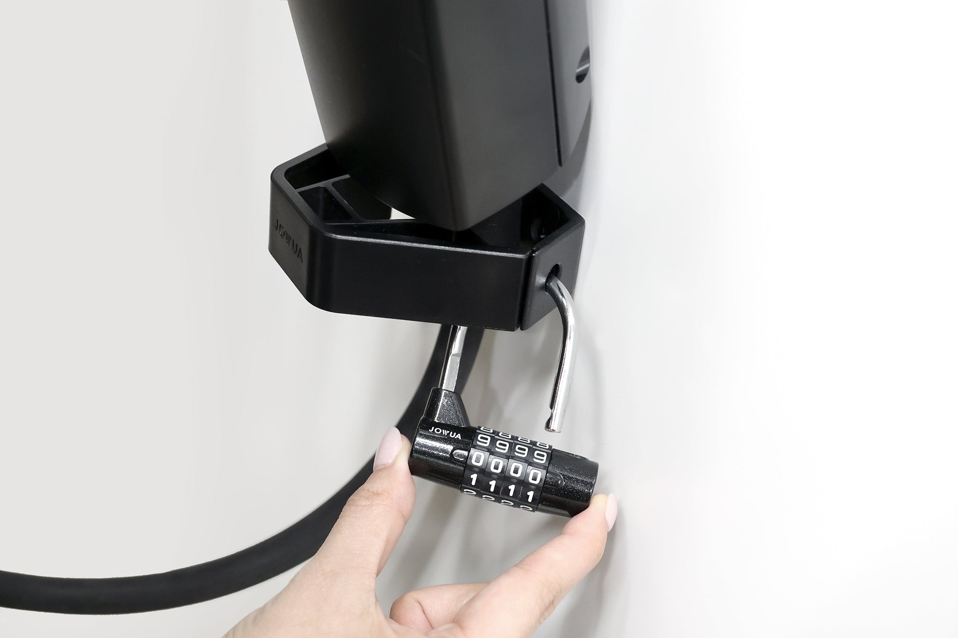 一隻手拿著 JOWUA Taiwan 防盜槍線固定整理器＋NEMA 14-50防水插座組合 (CCS2/CCS1/NACS)，使用黑色閂鎖旁的代碼 9999 鎖，將纜線固定到裝置上，背景為白色。.