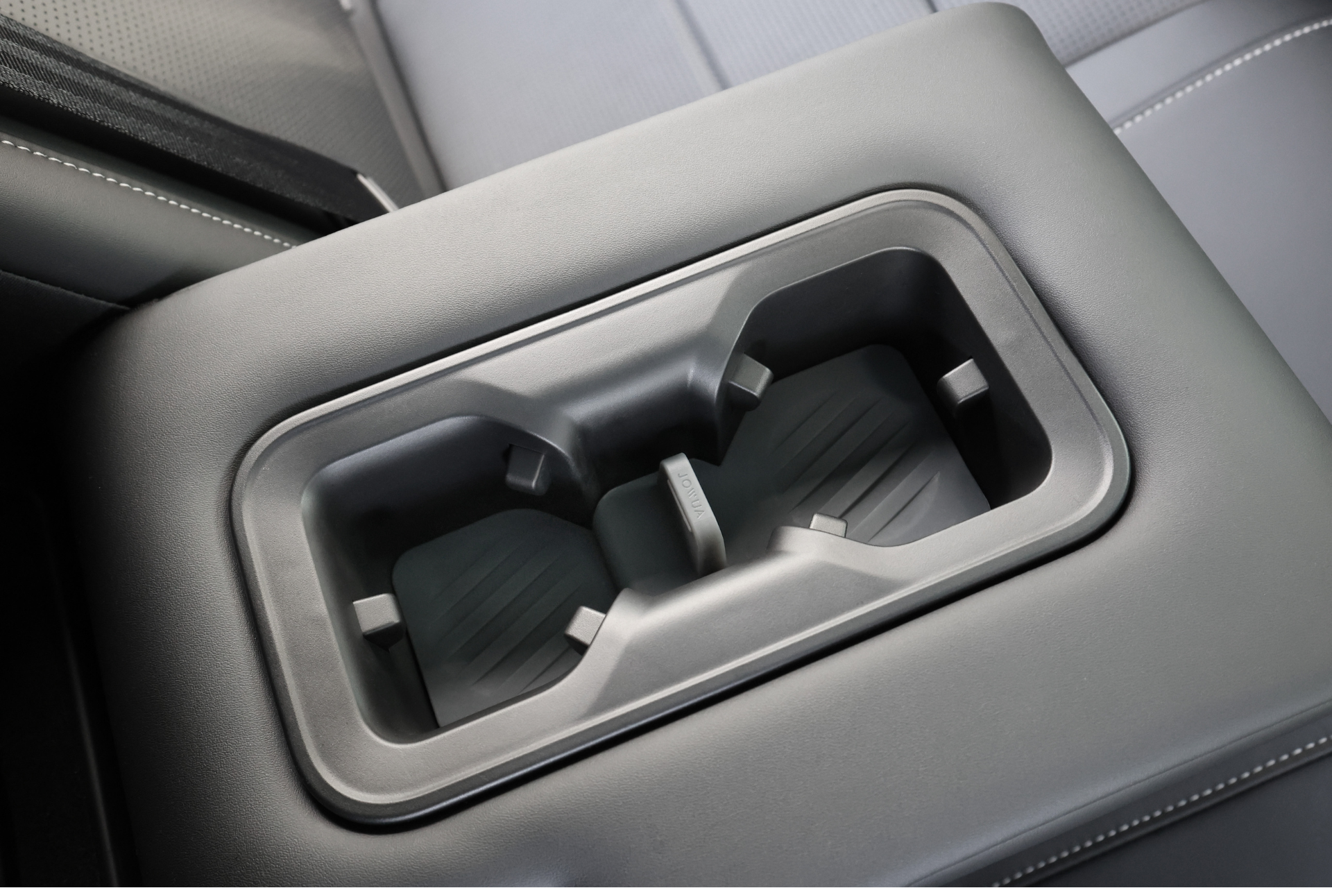 台灣 JOWUA 的 Foxtron Bria 後排杯墊特寫。黑色表面與皮革內裝的灰色縫線展現現代設計。.