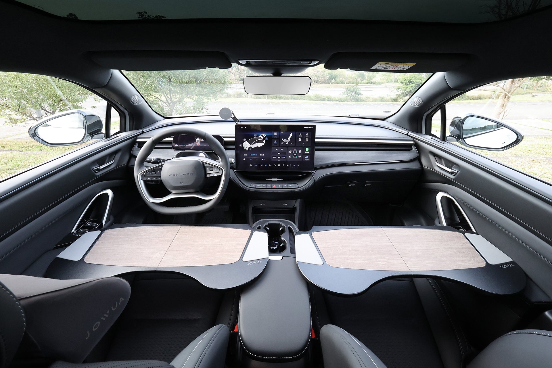 現代汽車內景，配備數位儀表板、大型觸控螢幕，以及 JOWUA Taiwan 車用折疊桌板作為前座上方的托盤桌，營造出行動辦公室的氛圍，陽光從車窗照射進來。.