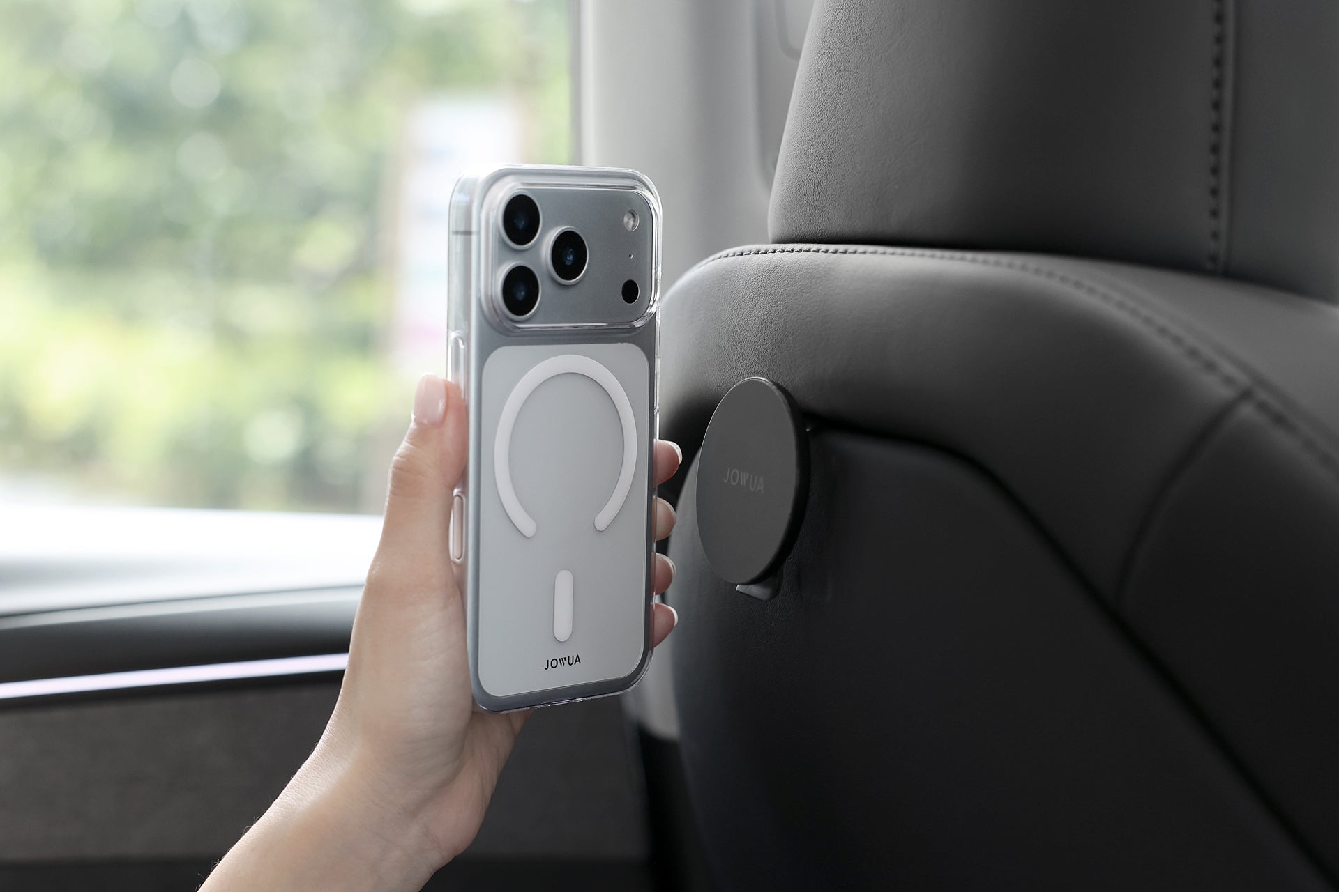 手持 JOWUA 台灣 MagSafe 保護殼 (iPhone 17 系列)，靠近頭枕上的磁性車座，突顯 iPhone 無線充電的便利性，外出時也能輕鬆使用。.