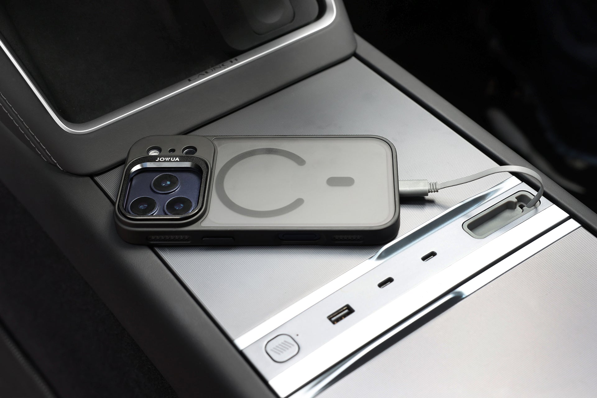 台灣 JOWUA MagSafe 保護殼 (iPhone 17 系列) 保護的智慧型手機正面朝下躺在汽車的現代金屬控制台上，透過 USB 連接線連接至控制台的連接埠，四周則是按鈕。.