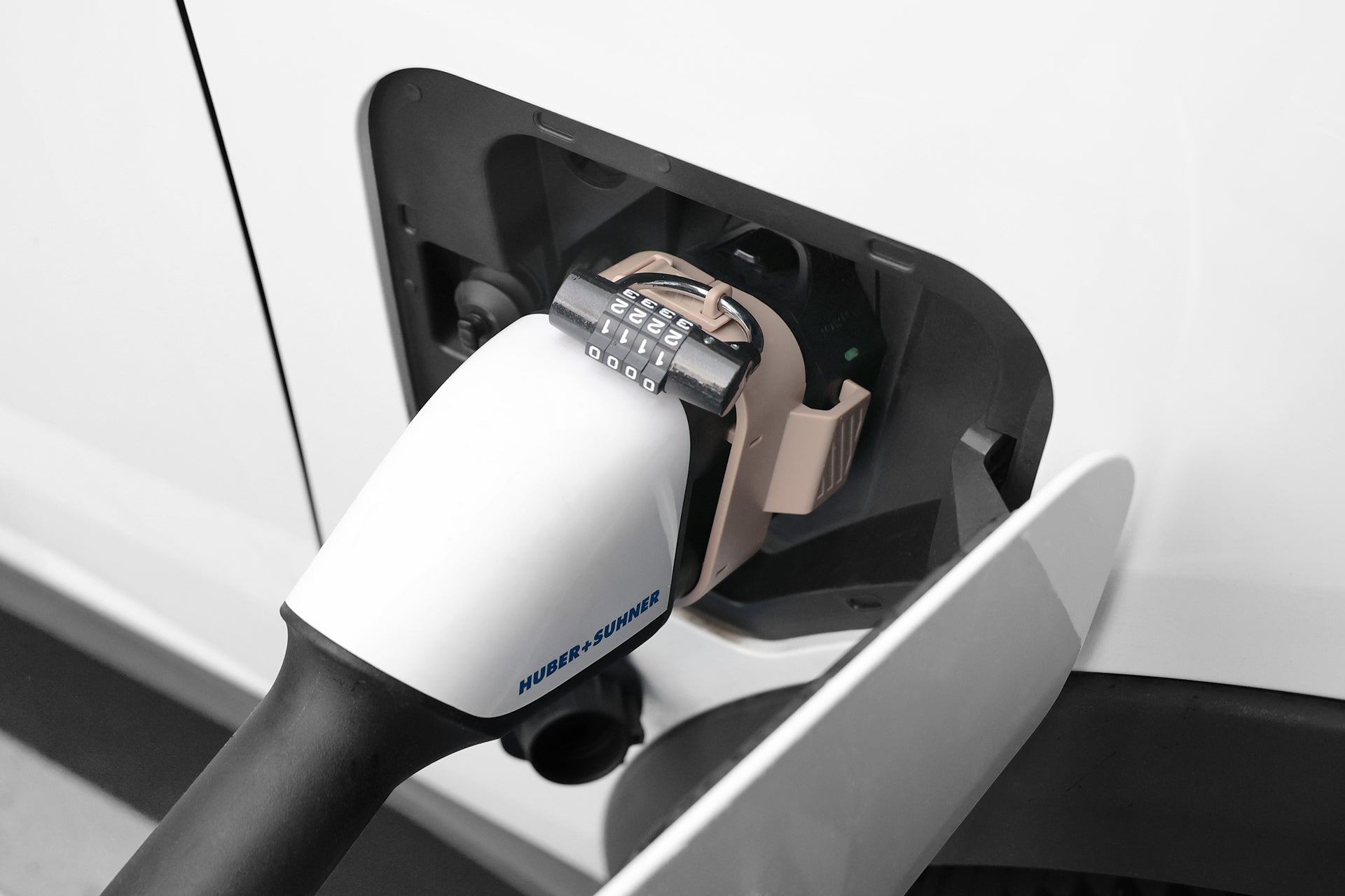 特寫圖顯示 JOWUA Taiwan CCS2 to CCS1 充電防拔鎖扣用掛鎖固定 CCS2 充電槍安全防拔槍，其 HUBER+SUHNER 插頭與電動車的白色外觀形成強烈對比。.