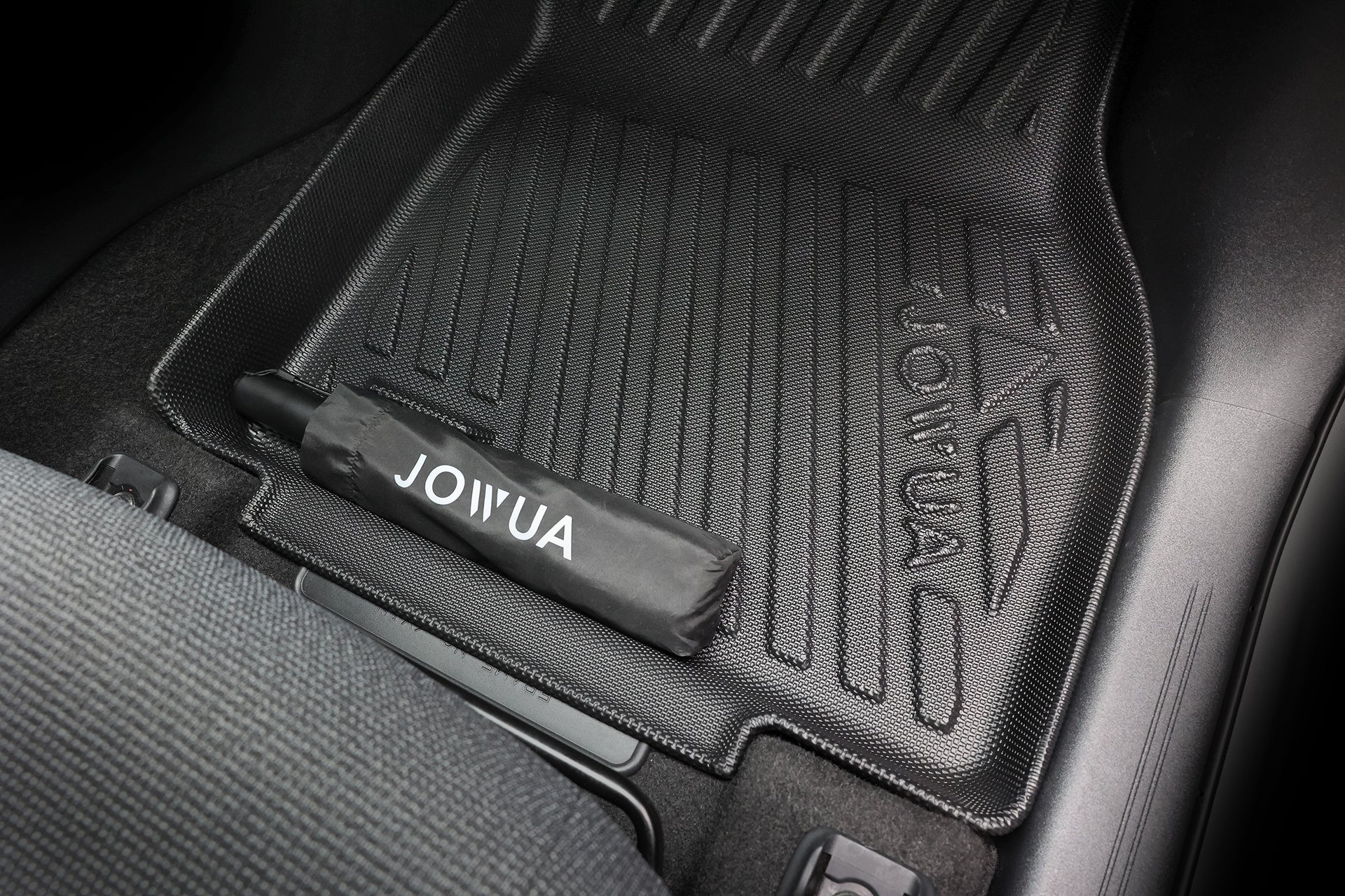 一把黑色的 JOWUA 雨傘，置於帶有紋理的黑色 JOWUA 台灣 立體防水腳踏墊（Toyota bZ4X）上，緊貼著車座邊緣。 這項專利汽車收納解決方案提供全面的整理功能，而具備全面防護功能的 JOWUA 台灣立體防水腳踏墊則能確保您的愛車獲得妥善保護。.