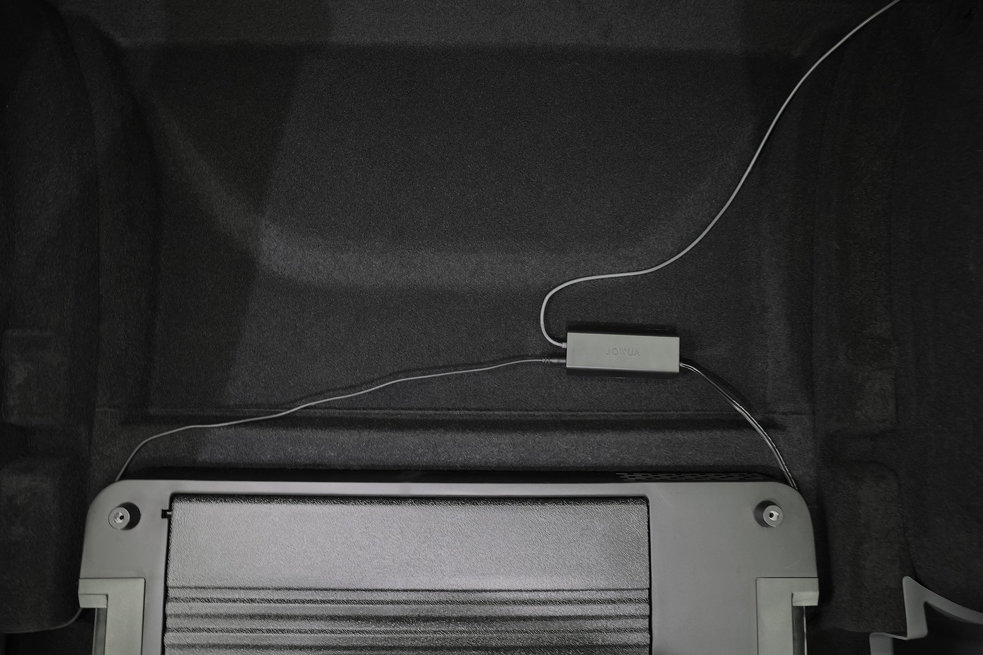 JOWUA Taiwan Type-C 車用行動冰箱 (Model Y全車系) 置於車廂內的黑色質感表面，可透過便利的Type-C電源讓物品保持冷卻。.