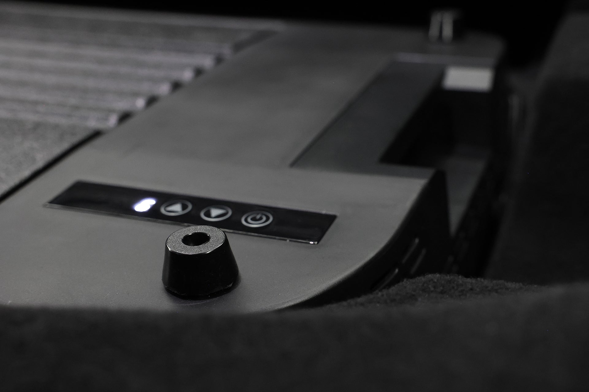 台灣 JOWUA Type-C 車用行動冰箱 (Model Y 全車系) 特寫，配備左/右箭頭和電源按鈕。前方的小型圓柱狀物體強調其 Type-C 供電功能。背景顯示裝置的模糊部分。.