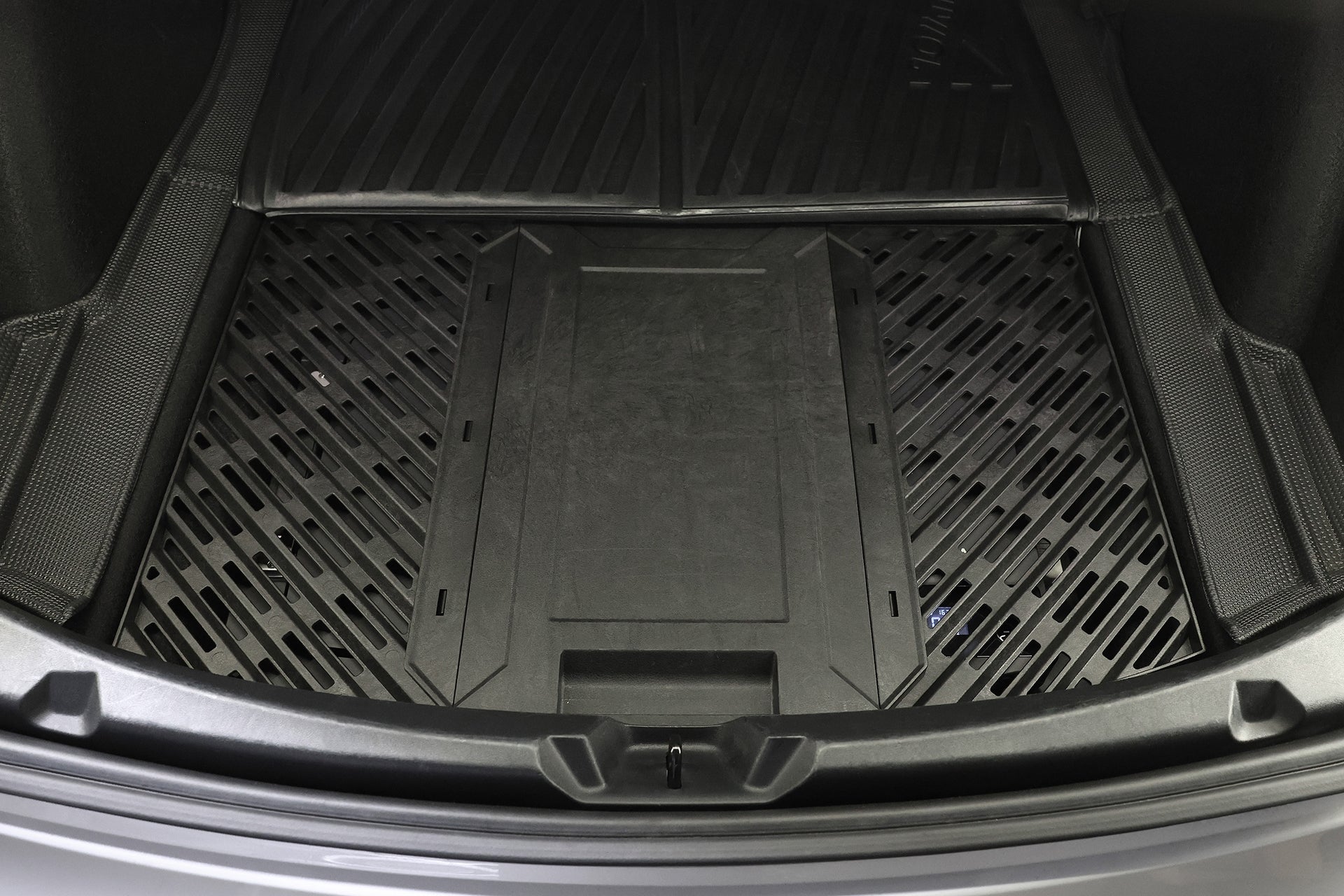 汽車行李箱特寫圖，內含黑色重型橡膠貨物墊，是安全運送 JOWUA Taiwan Type-C 車用行動冰箱 (Model 3 全車系) 的理想選擇，具備 Type-C 供電系統，並提供紋理板條和凸起邊緣的額外保護。.