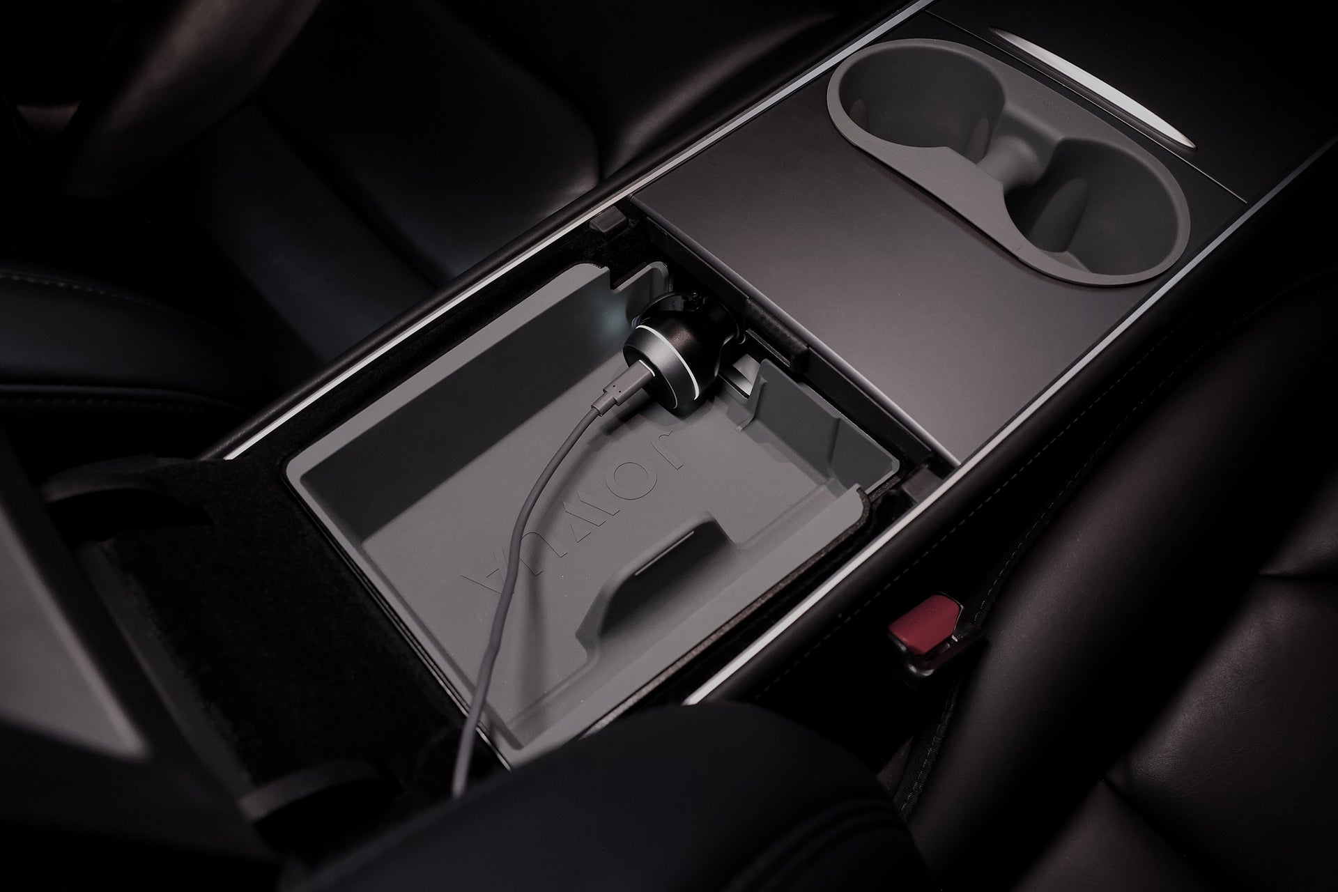 打開汽車中控台，可看到一個儲物格，內含連接 JOWUA Taiwan Type-C 車用行動冰箱 (Model 3 全車系) 的電源線，旁邊是杯架和黑色真皮座椅，非常適合隨身冷卻和裝置充電。.