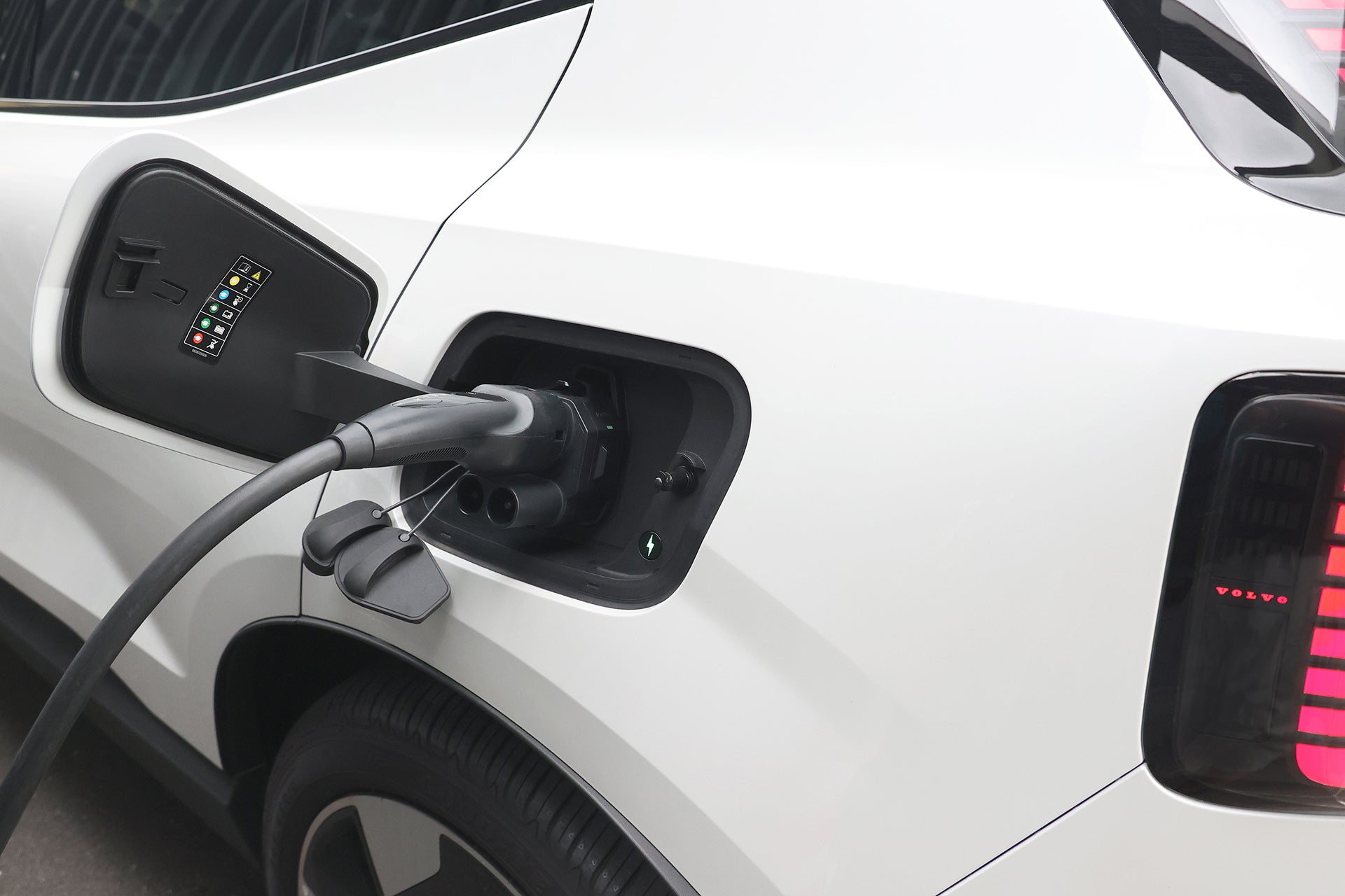 透過 JOWUA Taiwan 的 CCS1 快慢充萬用組充電的白色電動車特寫，充電線插入後輪附近的連接埠。.