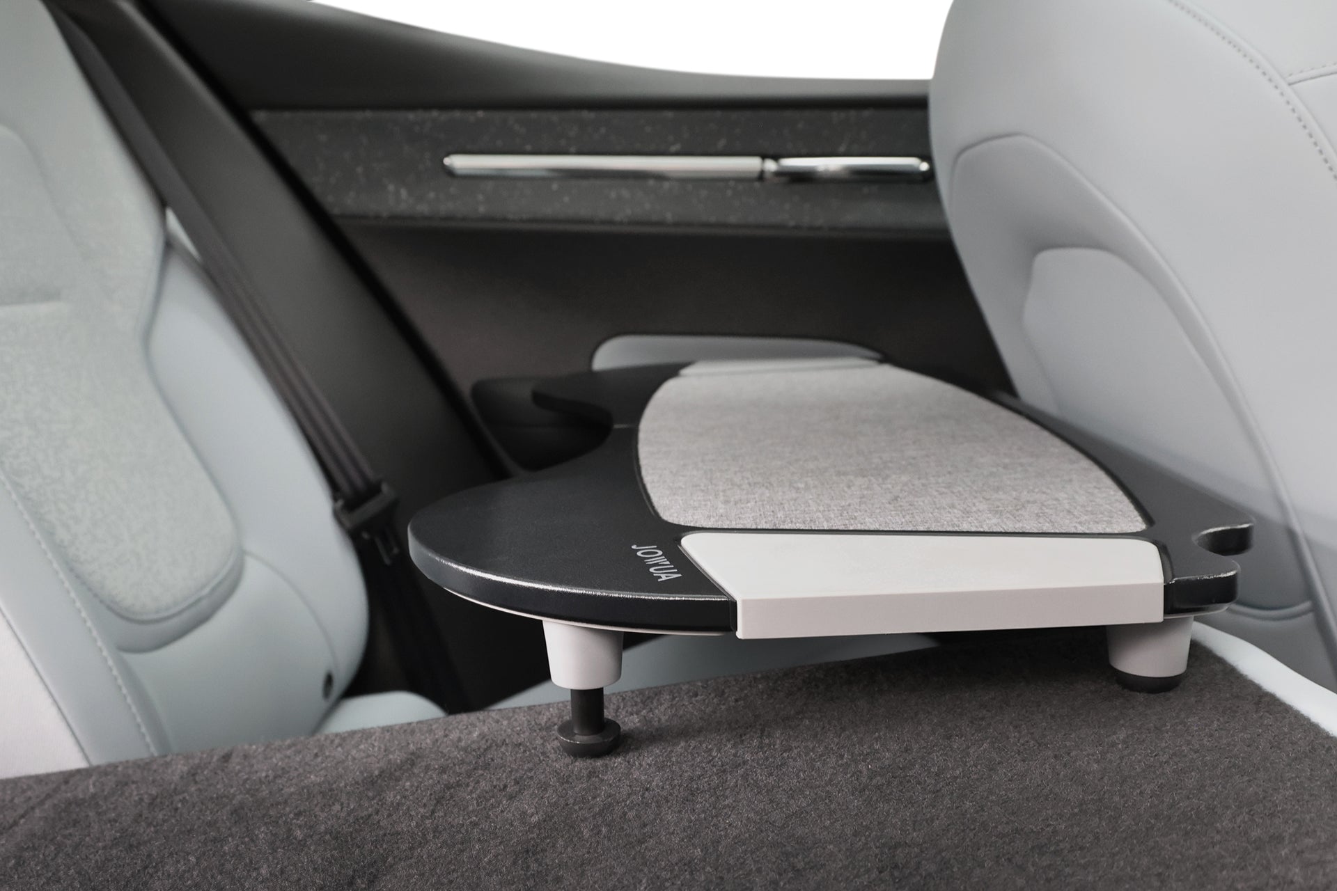 JOWUA Taiwan 車用折疊桌板是一款可拆卸、可摺疊的汽車座椅桌板，具有柔軟的紋理表面和可調整的桌腿，專為淺灰色裝潢的現代汽車後座而設計。.