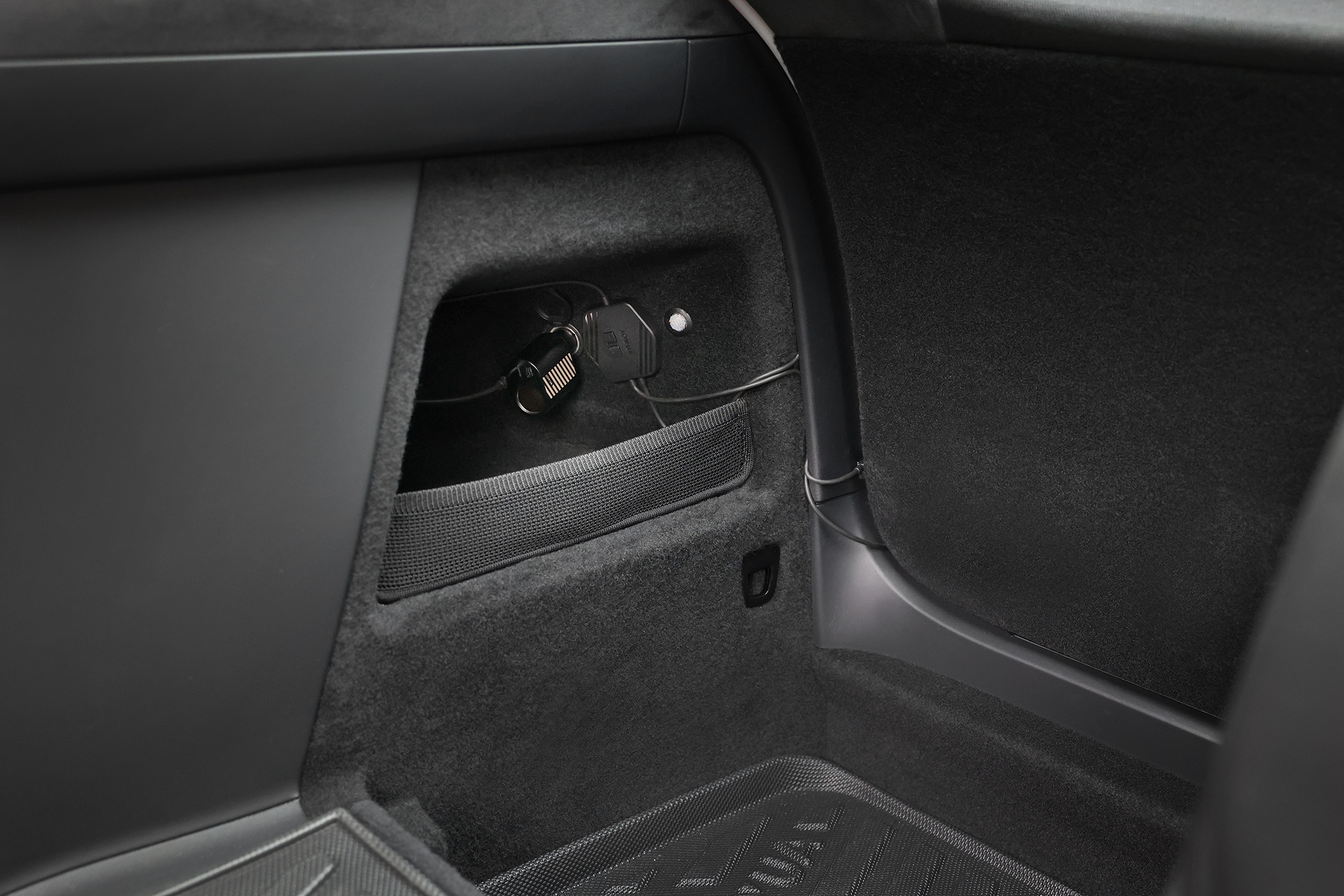 台灣 JOWUA 後車廂氣氛燈｜真言套索 (Model X) 在汽車後方內裝的特寫，有一個小的儲物格，插上充電線的 Type-C 擴充點菸器，以及地板和側板的深色地毯。.