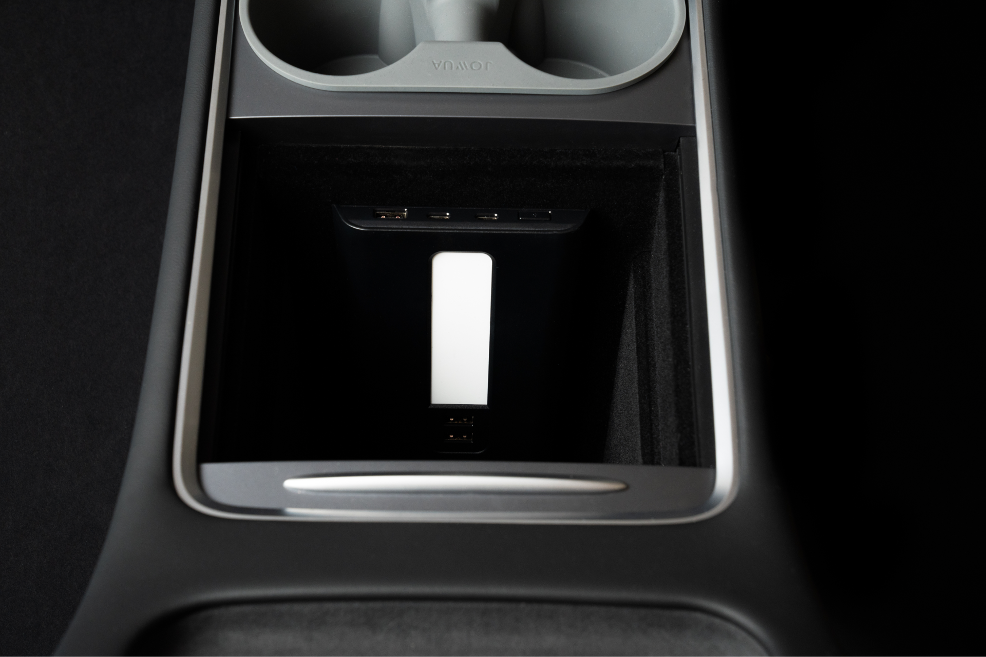 汽車的中控台（可能來自 Model 3 或 Model Y）具有一個帶有多個 USB 連接埠的儲物箱，後面板上有一個白色矩形標籤。它被優雅的黑色和銀色裝飾包圍，是 JOWUA 台灣 45W LED 中控組合的一部分。.