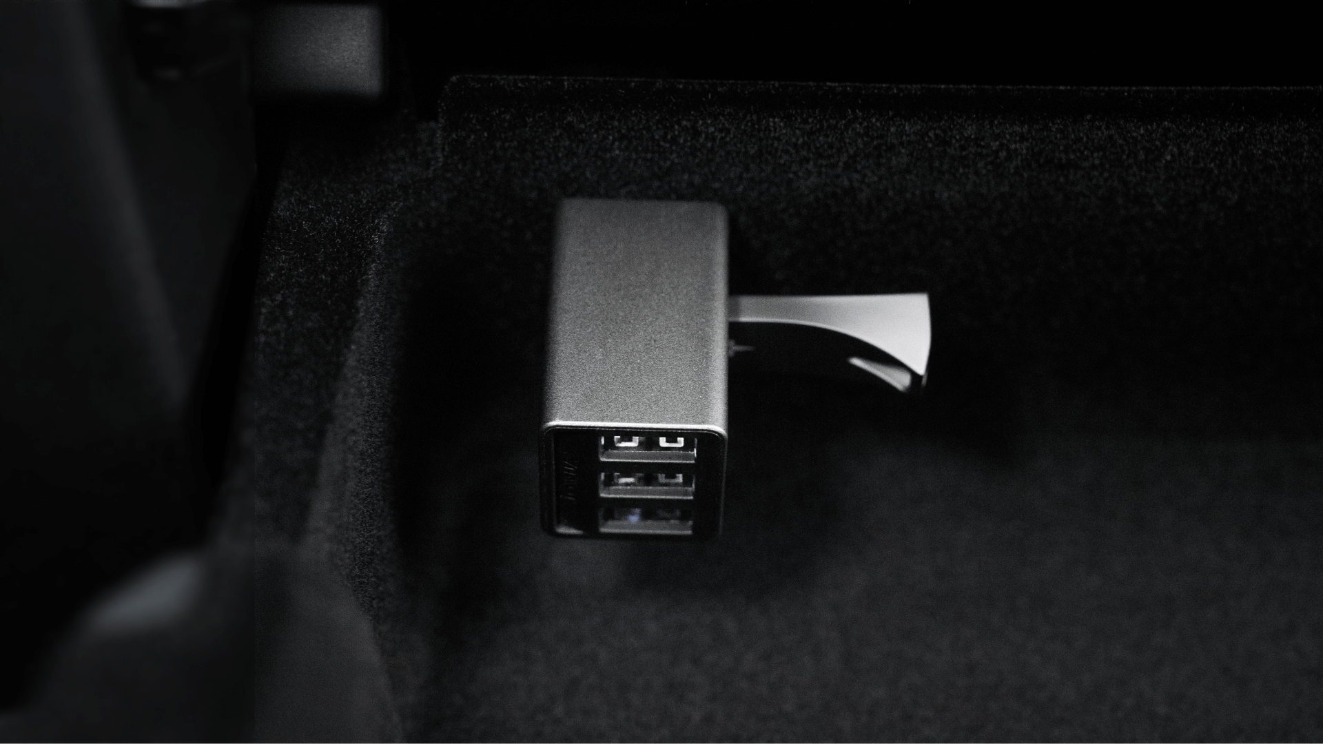 JOWUA Taiwan 36W 數據組合 USB 集線器插入黑色表面的插座的特寫，該插座具有多個端口，可插入 USB 記憶棒。深色紋理氛圍與特斯拉 Model 3/Y 光滑的內裝氛圍相得益彰。.
