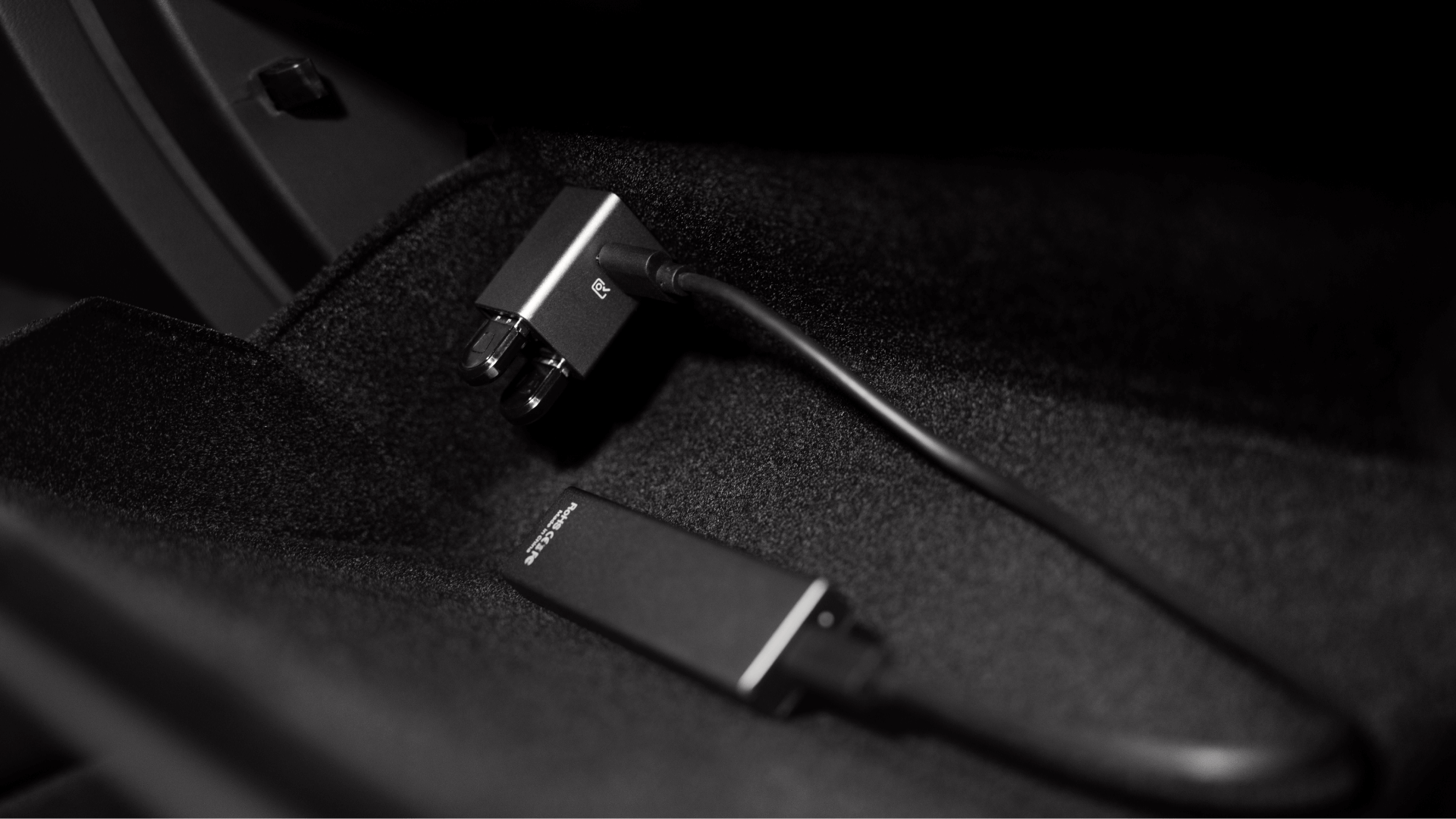 黑白影像顯示了特斯拉 Model 3/Y 內部深色紋理表面上的 JOWUA 台灣 36W 資料組合數位電纜。這條電纜具有矩形連接器，一個是直的，另一個是 L 形，非常適合 USB 集線器連接或快充（快速充電）。.