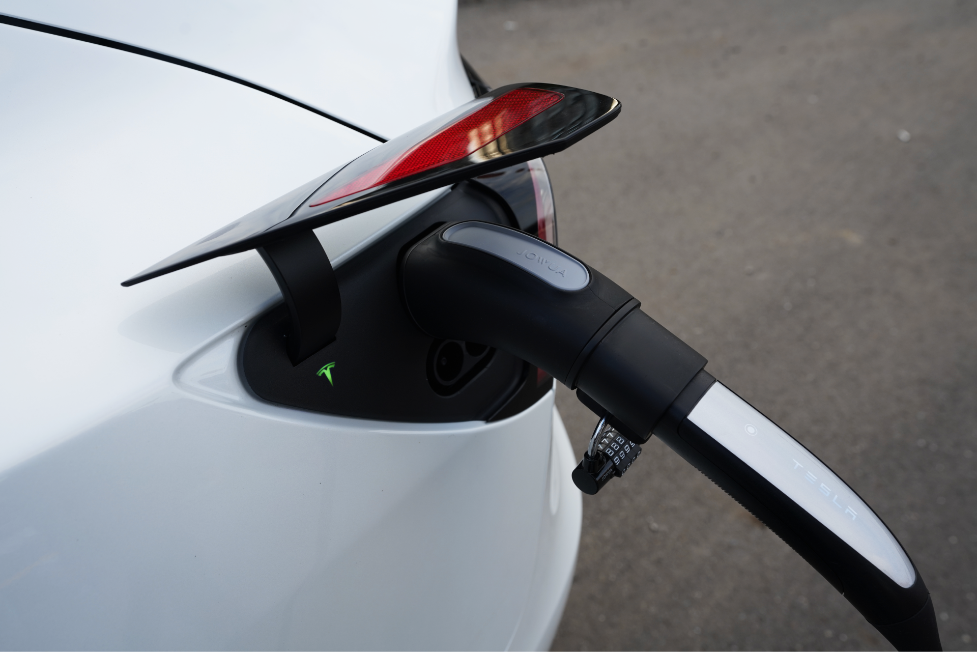 一輛白色電動車正在使用 JOWUA 台灣 TPC(NACS) 轉 CCS2-AC (TYPE2) 轉接器充電，並具有 IP65 防水功能。充電埠是開放的，透過電纜連接，而尾燈和一個小綠燈在瀝青地面上閃閃發光。.